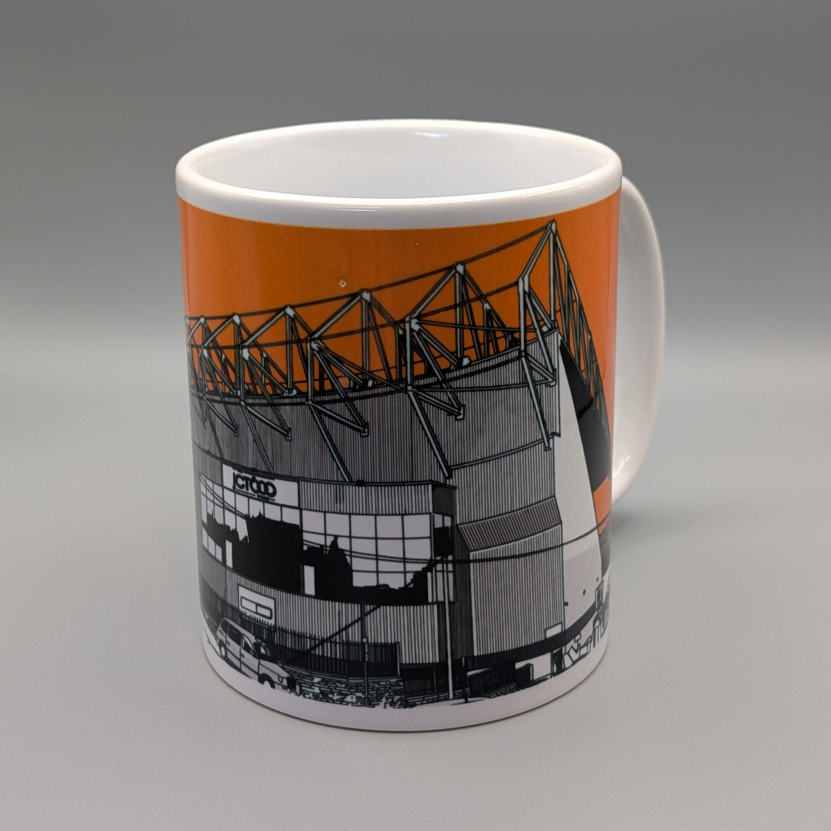 A white ceramic mug featuring a printed graphic of a stadium with an orange background and black-and-white architectural illustration, shown on a gray gradient background.