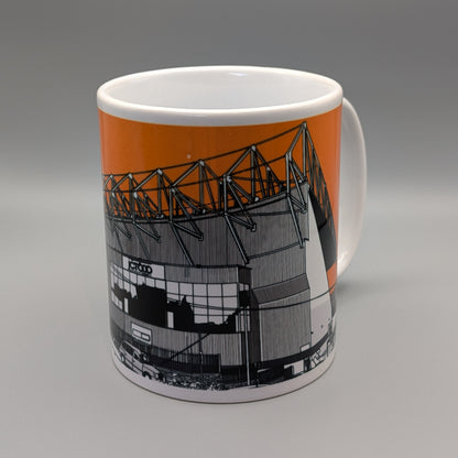 A white ceramic mug featuring a printed graphic of a stadium with an orange background and black-and-white architectural illustration, shown on a gray gradient background.