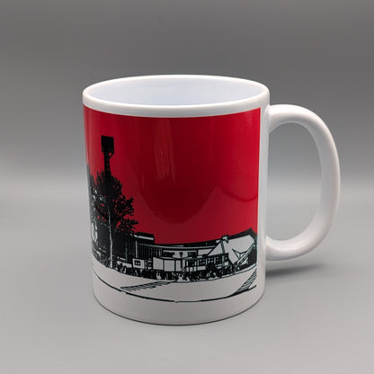 A white ceramic mug with a printed graphic of a street scene under a solid red sky, shown on a neutral gray background.