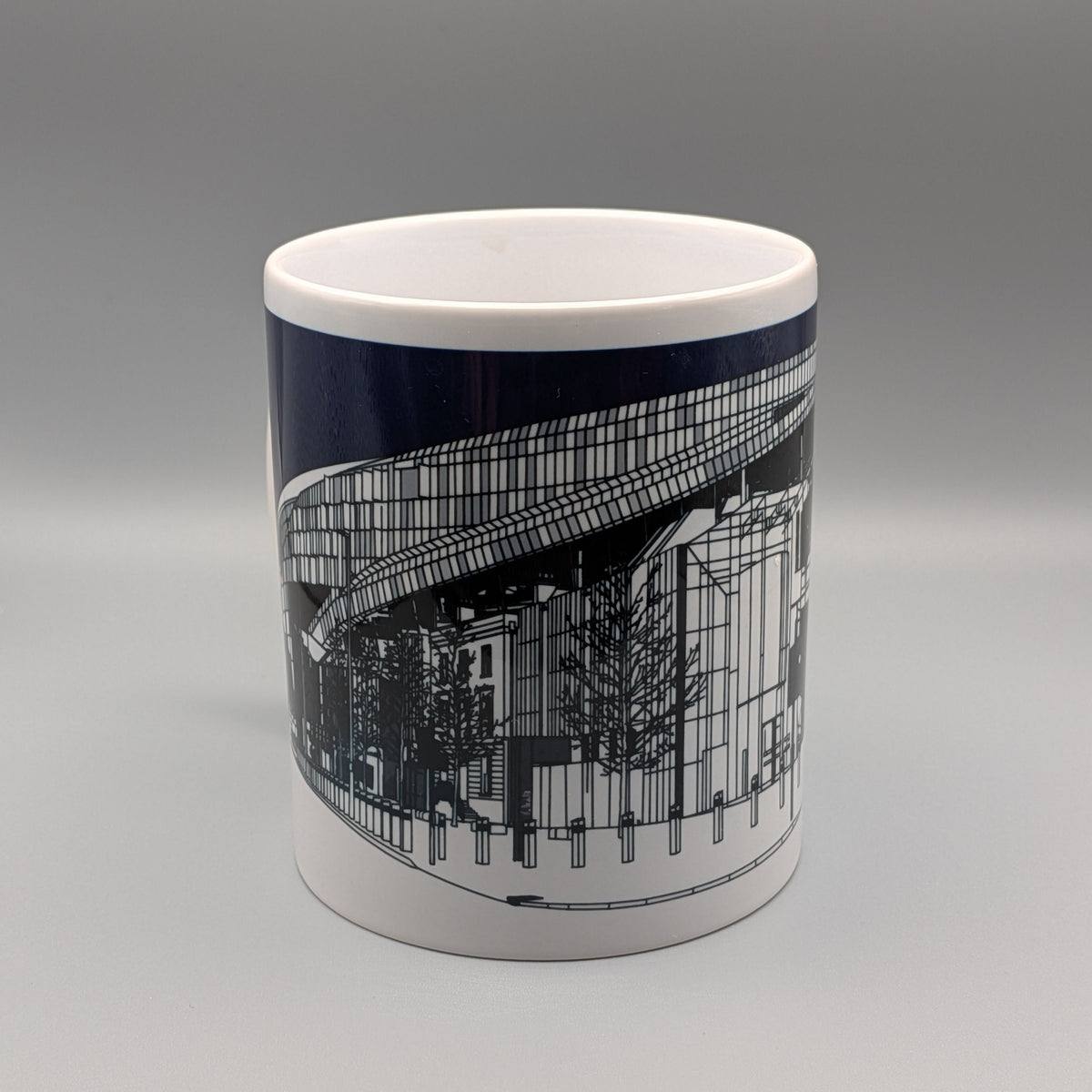 A white ceramic mug featuring a detailed black architectural line drawing of a modern building on the side, photographed against a neutral gray studio background.