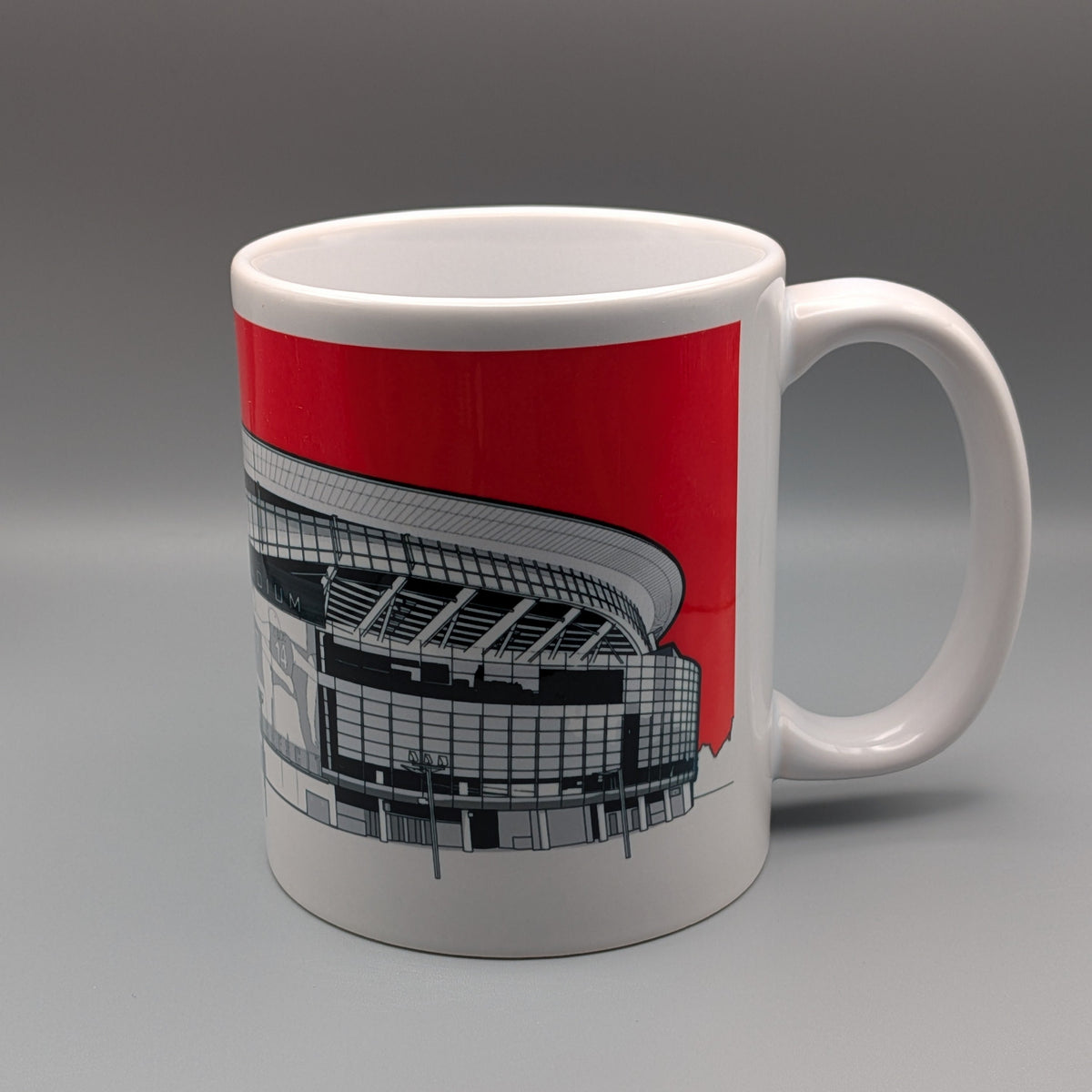 A white ceramic mug featuring a graphic print of a stadium under a bold red sky, set against a neutral gray studio background.